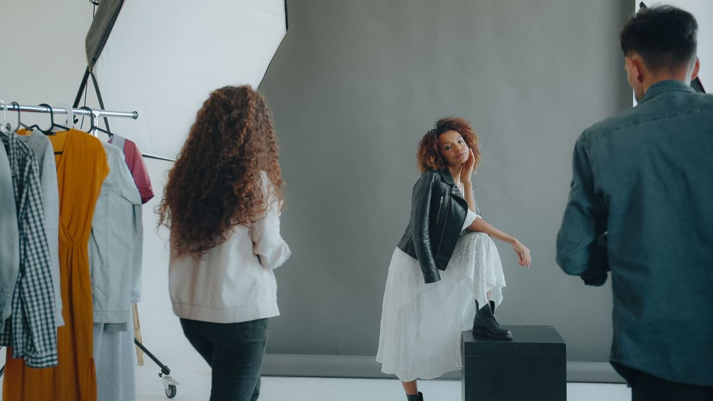 Fashion studio shoot with model posing and photographer and stylist in action.
